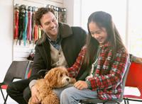 father and daughter smiling petting brown furry doodle dog