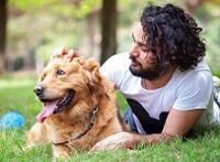 man with black curly hair laying on grass with his hand on his golden retriever